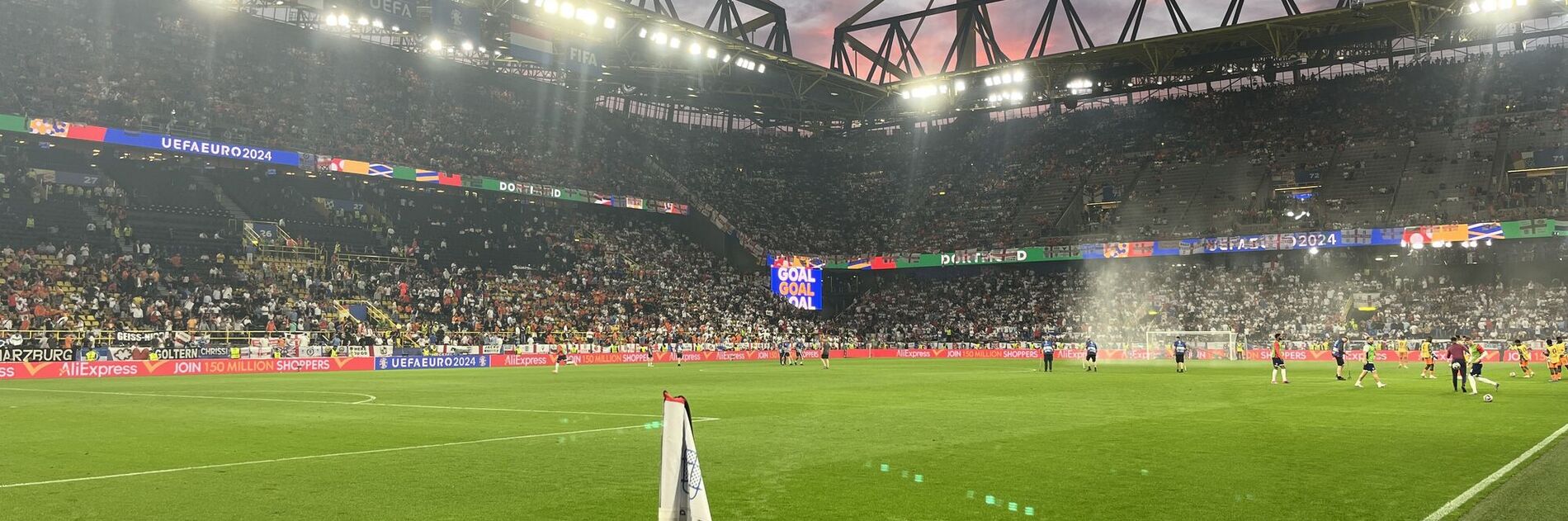 Fußballstadion mit Naturrasenplatz, Flutlichtanlage und gefüllten Zuschauerrängen während eines Spiels (KI-generiert)