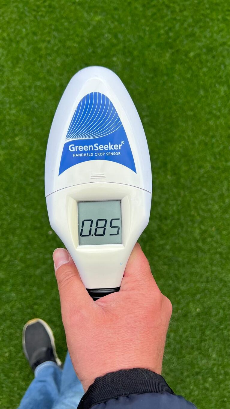 Handheld-Gerät mit Display und Sensor zur Vegetationsanalyse über einer Rasenfläche, zeigt numerischen Wert an (KI-generiert)