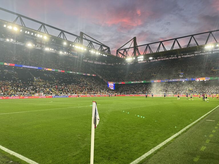 Fußballstadion mit Naturrasenplatz, Flutlichtanlage und gefüllten Zuschauerrängen bei einem Spiel unter künstlicher Beleuchtung (KI-generiert)