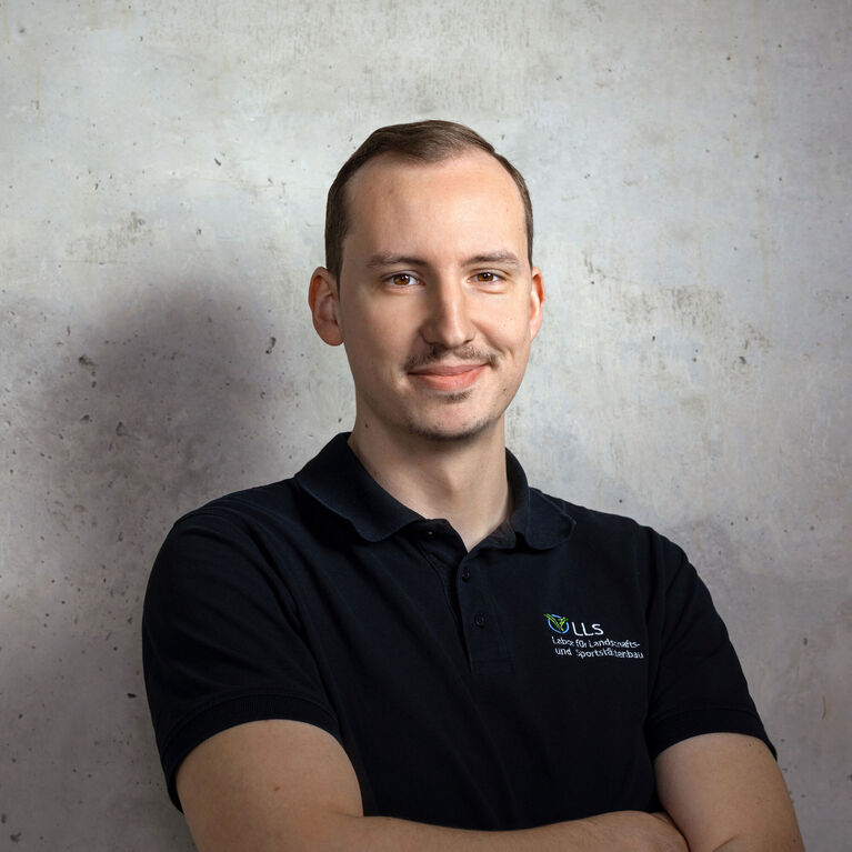 Mann mit kurzen Haaren in dunklem Poloshirt mit Firmenlogo vor unscharfem Betonhintergrund (KI-generiert)